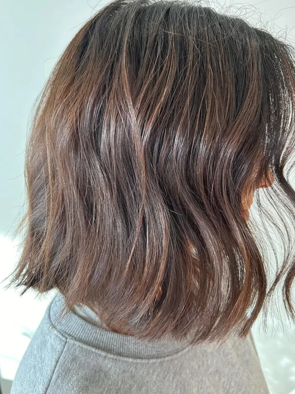 A textured, shoulder-grazing brunette bob with soft waves, cut by Amy Kurtz